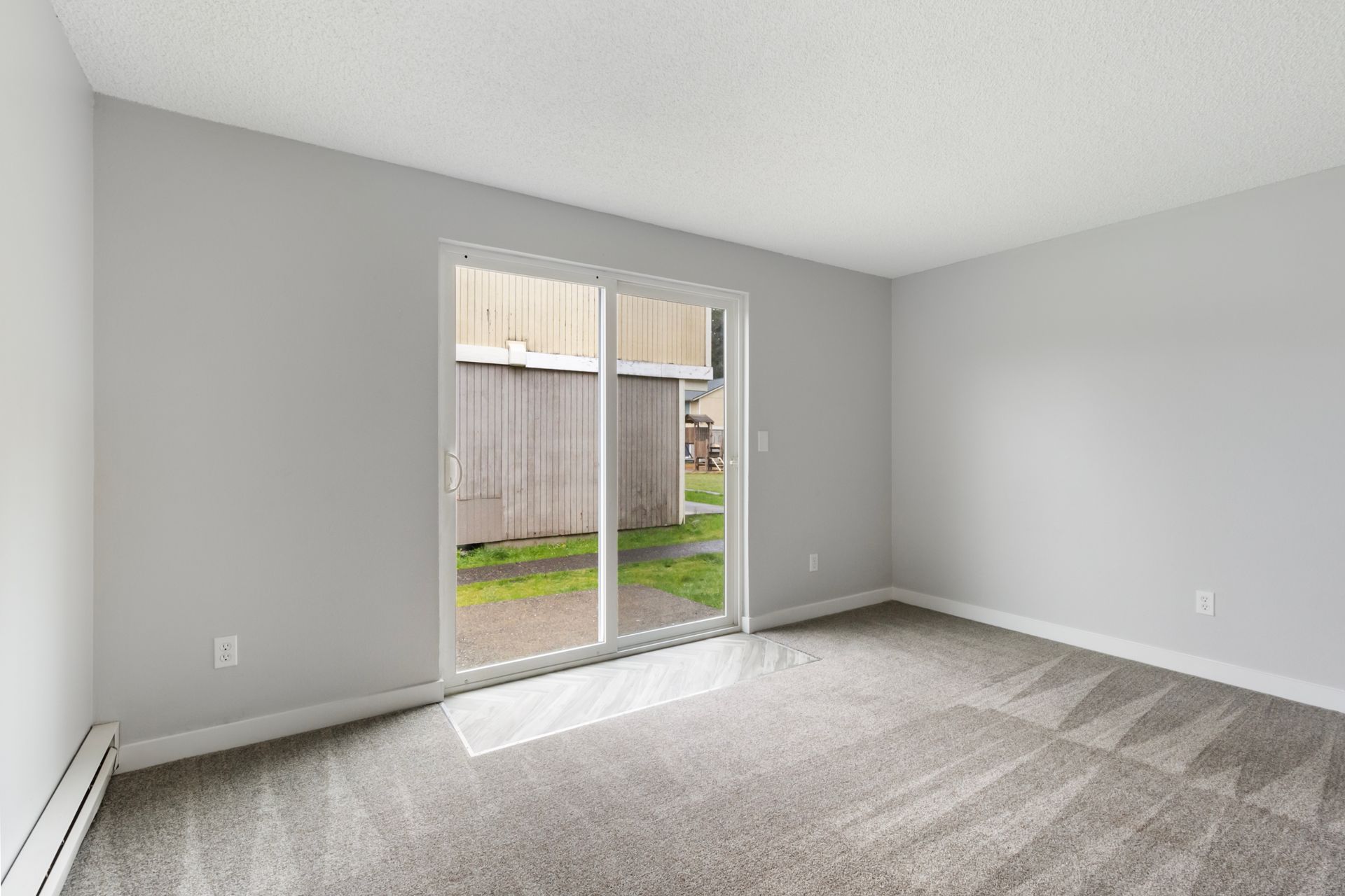 An empty living room with a sliding glass door leading to a patio.