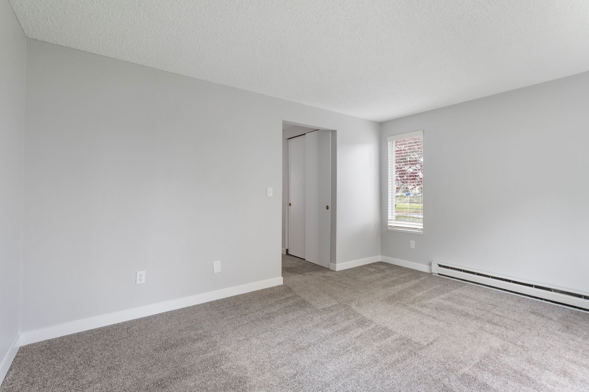 An empty living room with a carpeted floor and a window.
