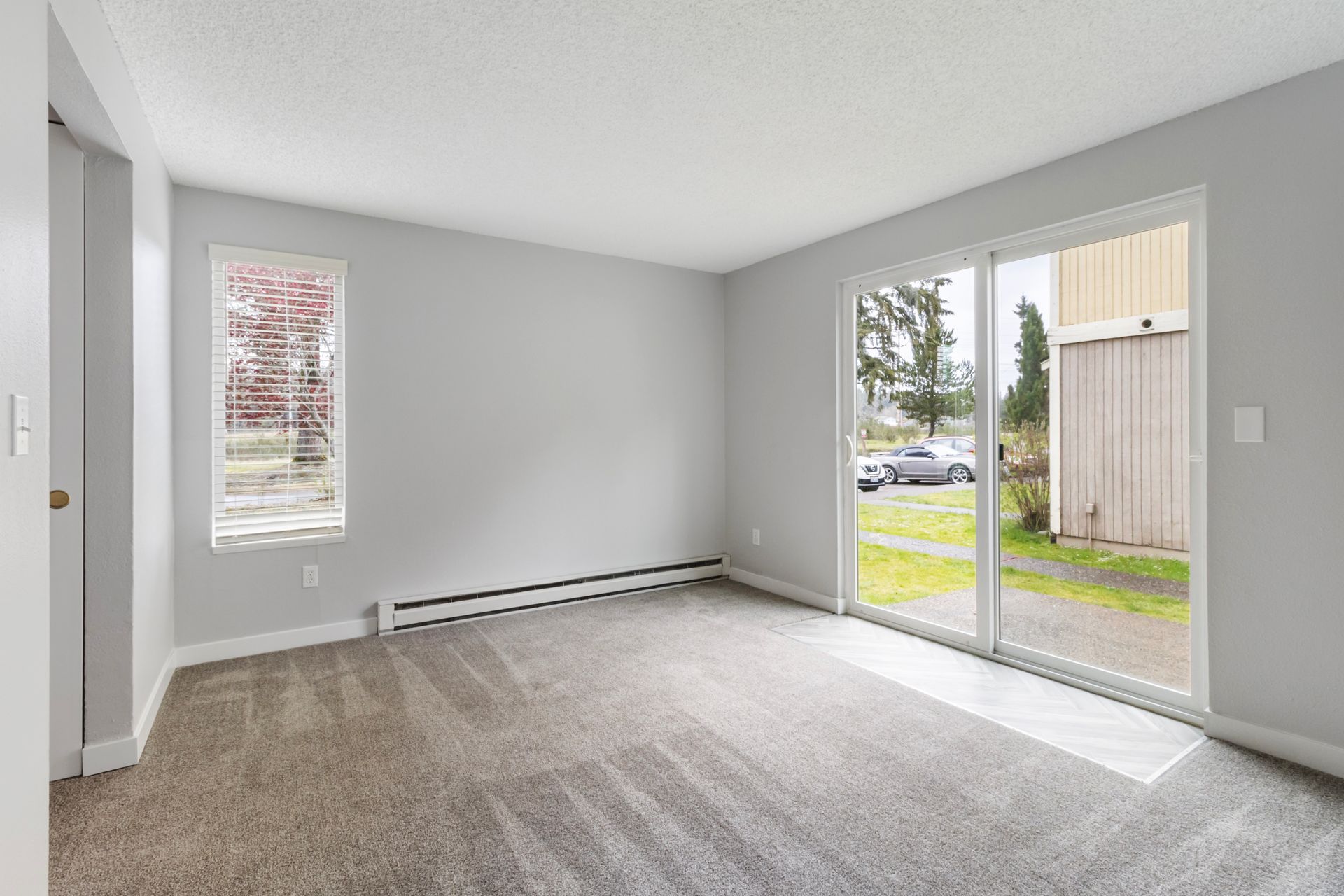 An empty living room with a sliding glass door and two windows.
