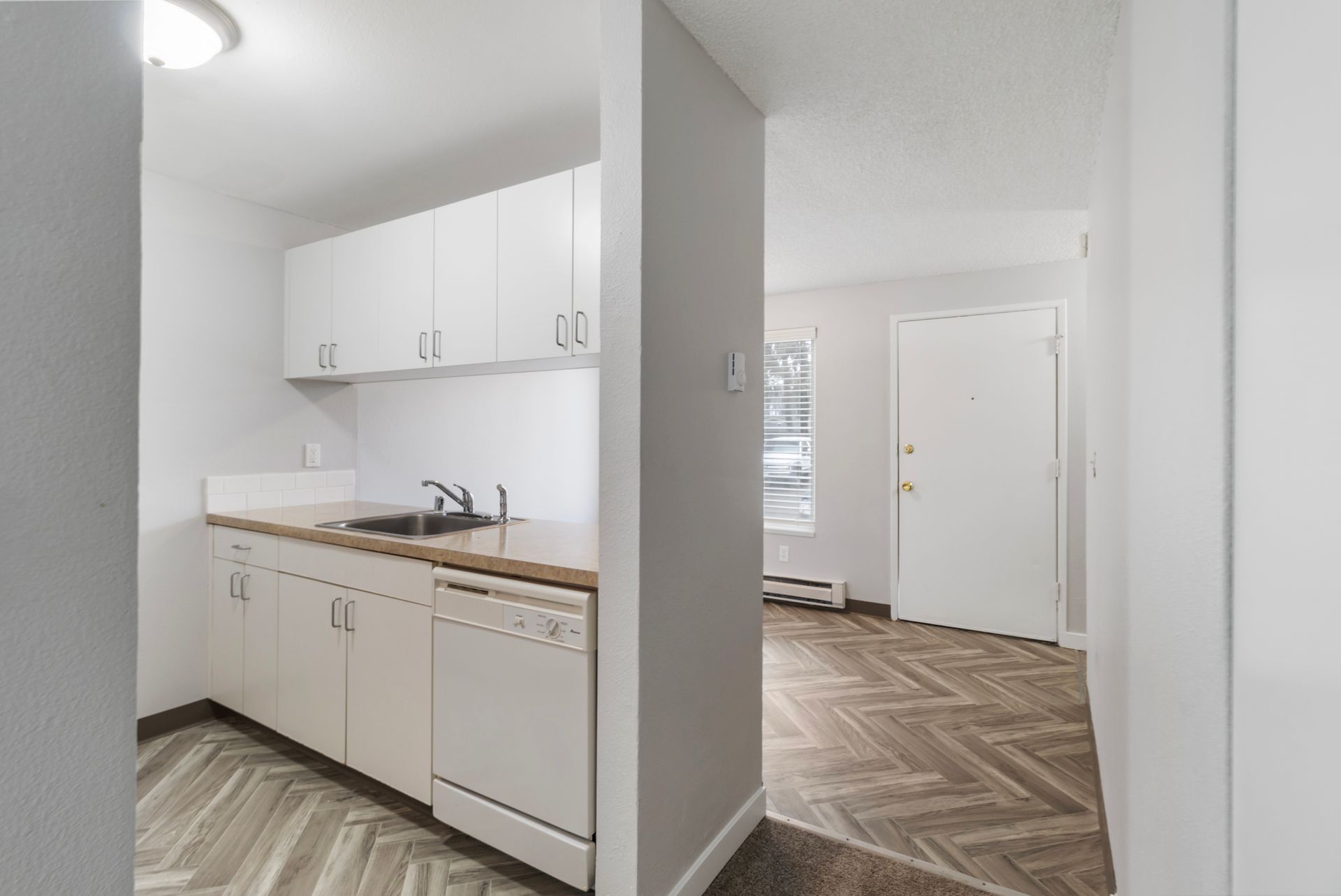 A kitchen with white cabinets , a sink , and a dishwasher.