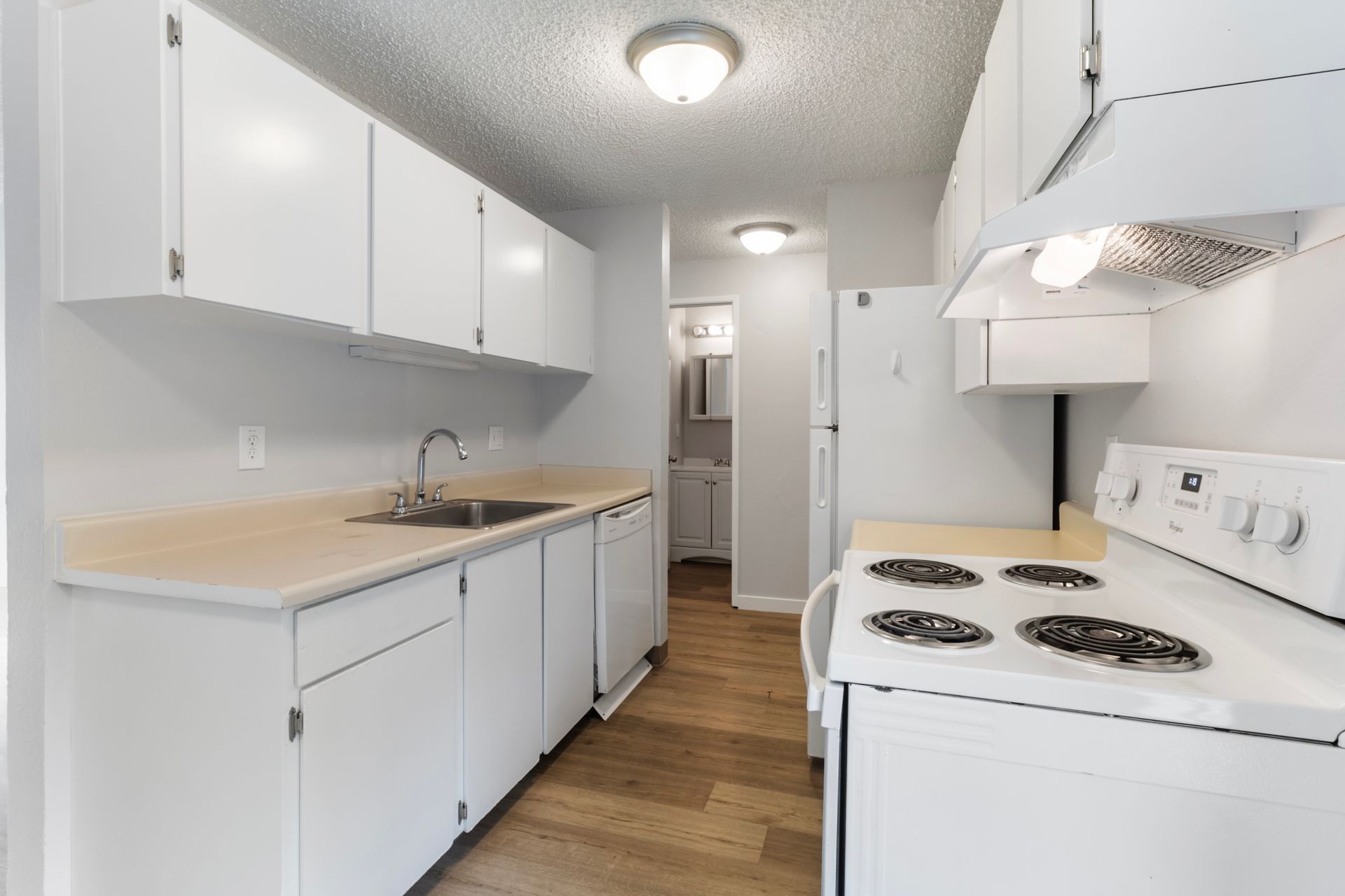A kitchen with white cabinets , a stove , a sink , and a refrigerator.