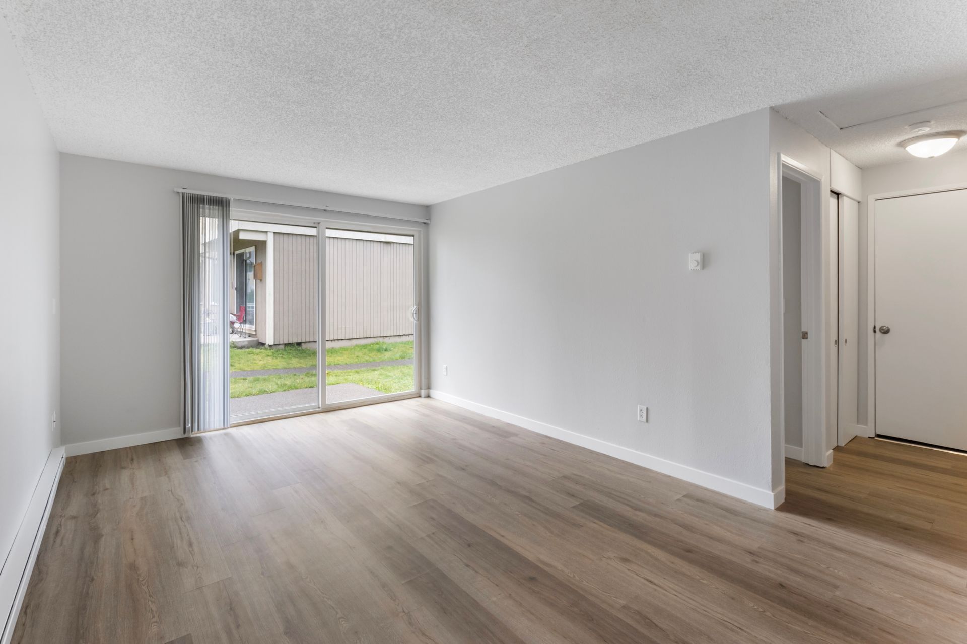 An empty living room with hardwood floors and sliding glass doors.