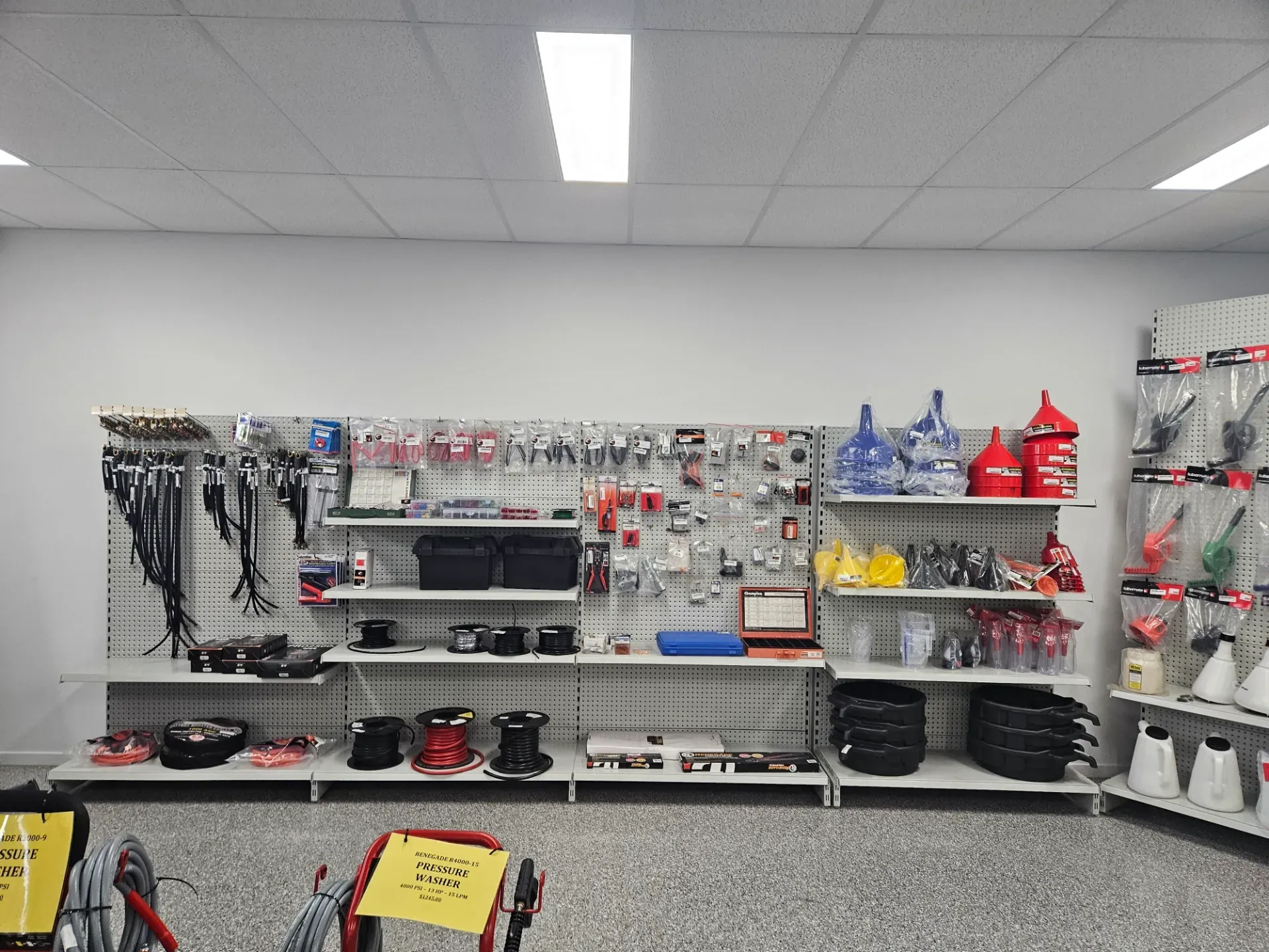 A well-lit retail store aisle showing shelves stocked with various tools, automotive supplies, and colorful funnels.