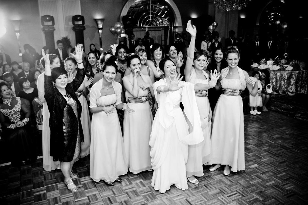 A black and white photo of a bride and her bridesmaids dancing at a wedding reception.