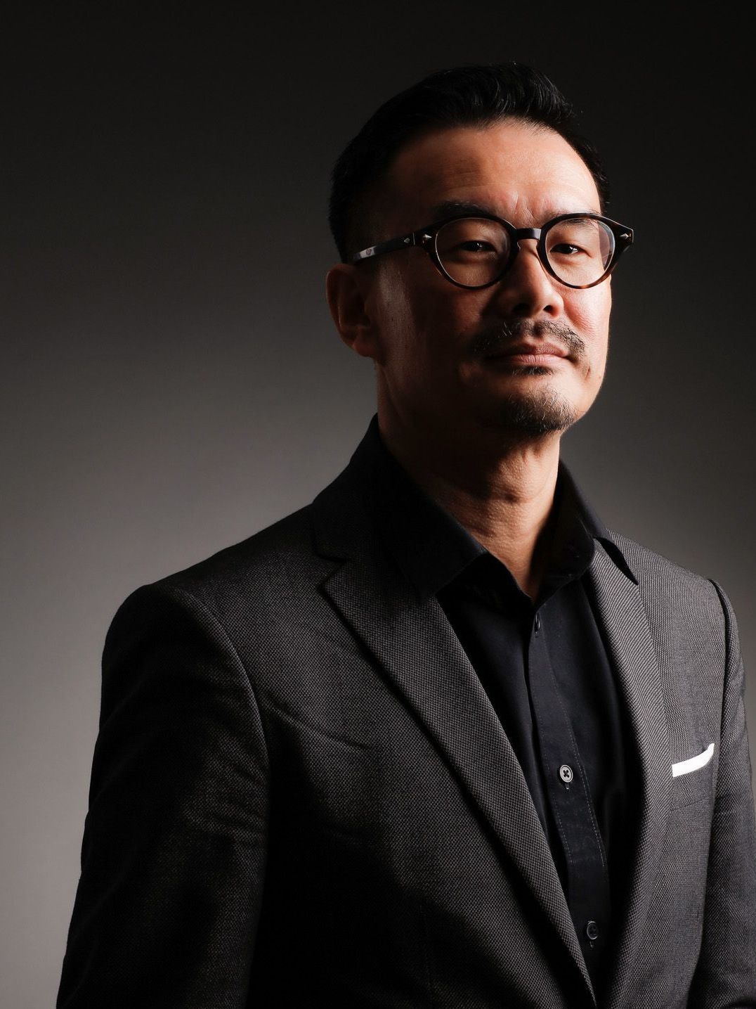 A man in a suit and glasses is looking at the camera.