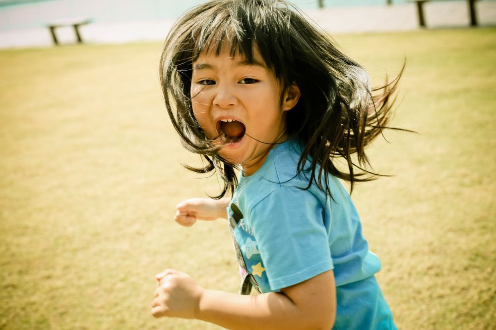 A little girl is running in a field with her mouth open.