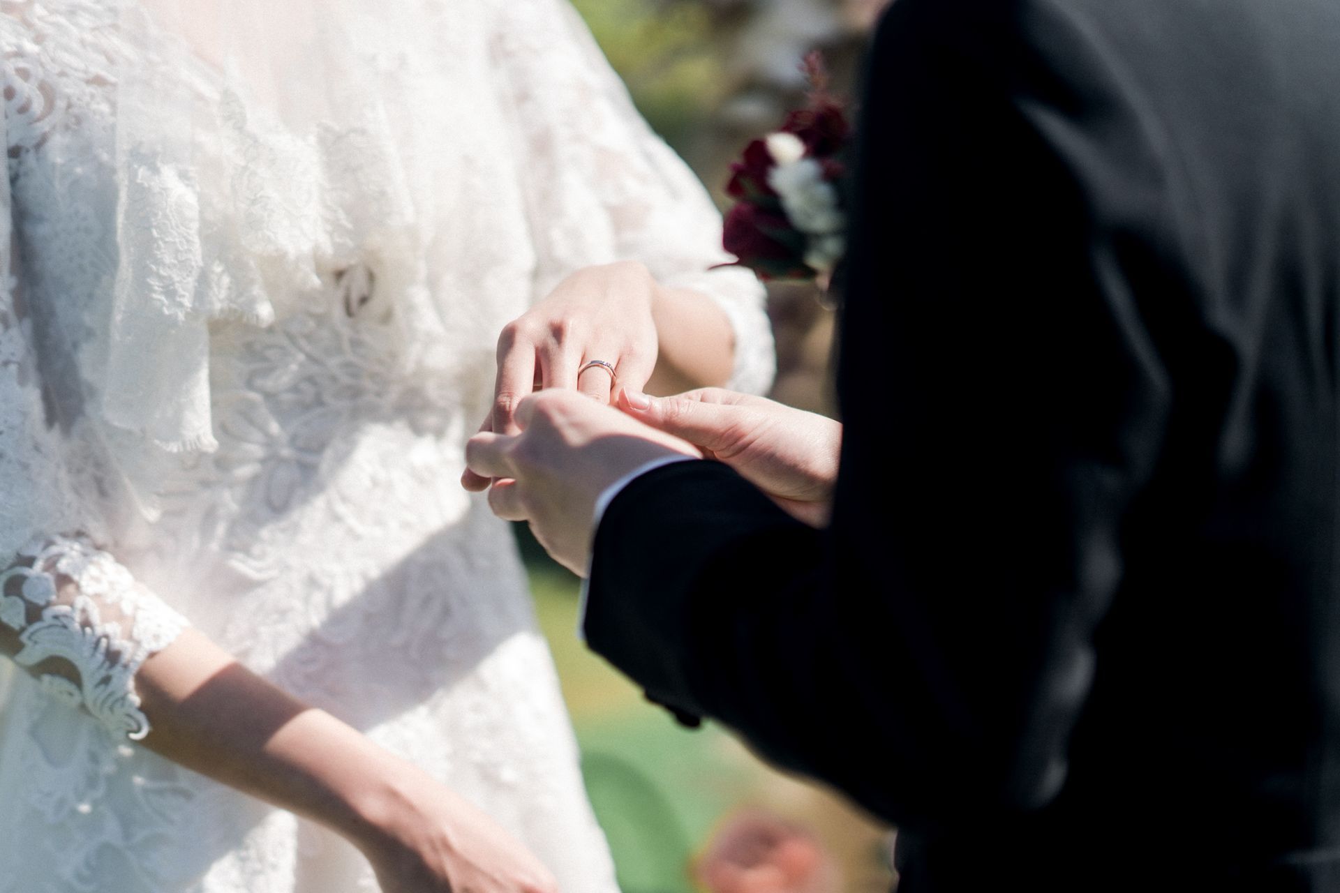 A bride and groom are getting married and the groom is putting a wedding ring on the bride 's finger.