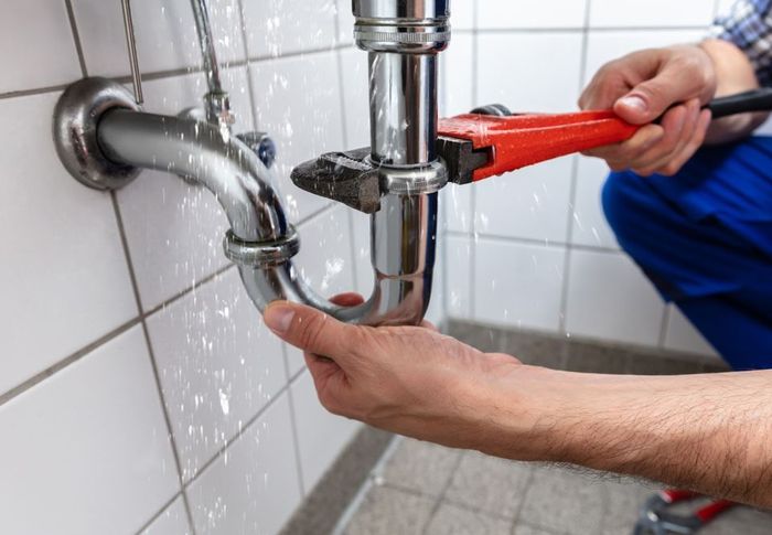 A plumber is fixing a pipe in a bathroom with a wrench