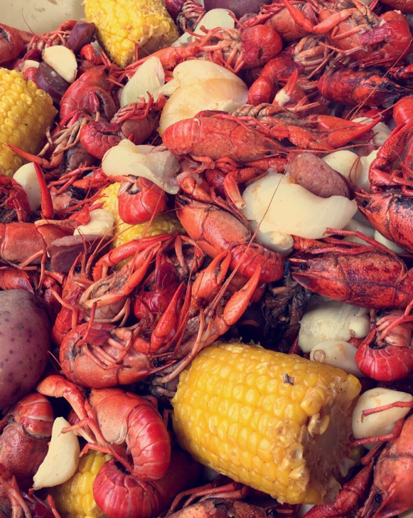 A close up of a crawfish boil with corn on the cob and potatoes.