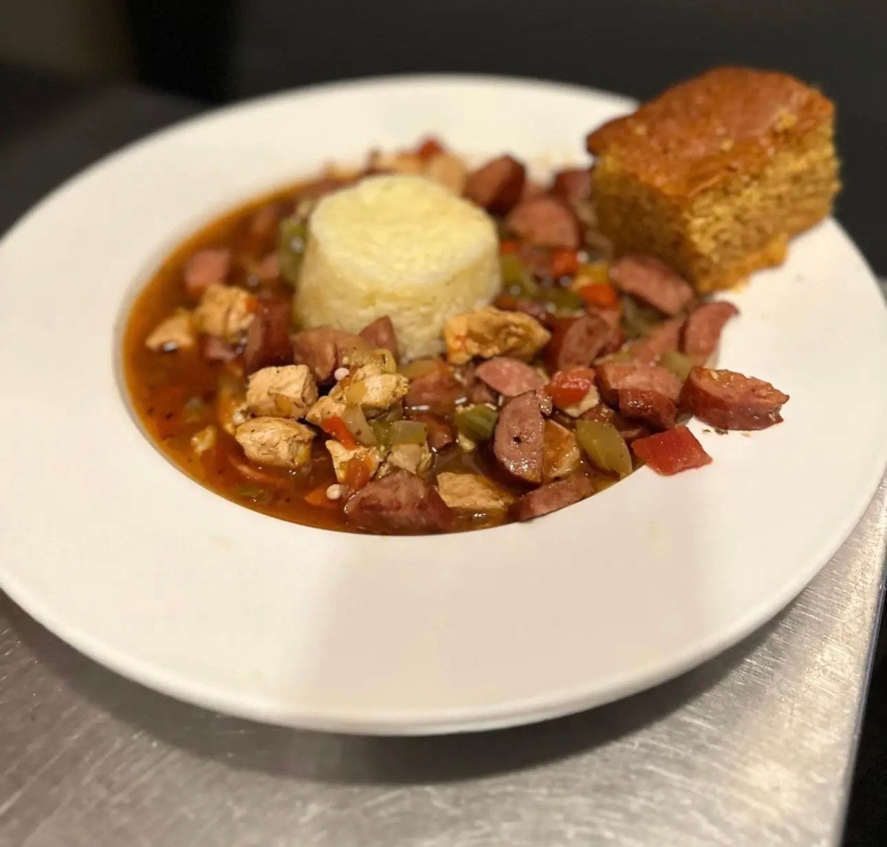 A white plate topped with a bowl of food and a piece of cornbread.