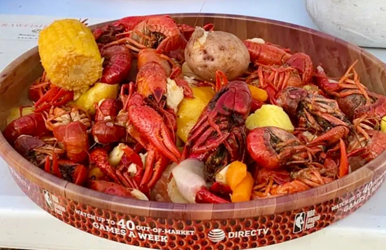 A wooden bowl filled with crawfish , potatoes and corn on the cob.