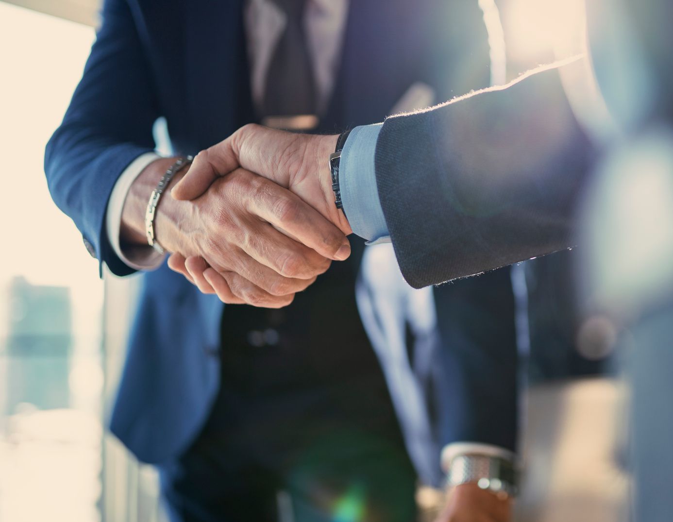 Two men in suits shaking hands in a bright office setting.
