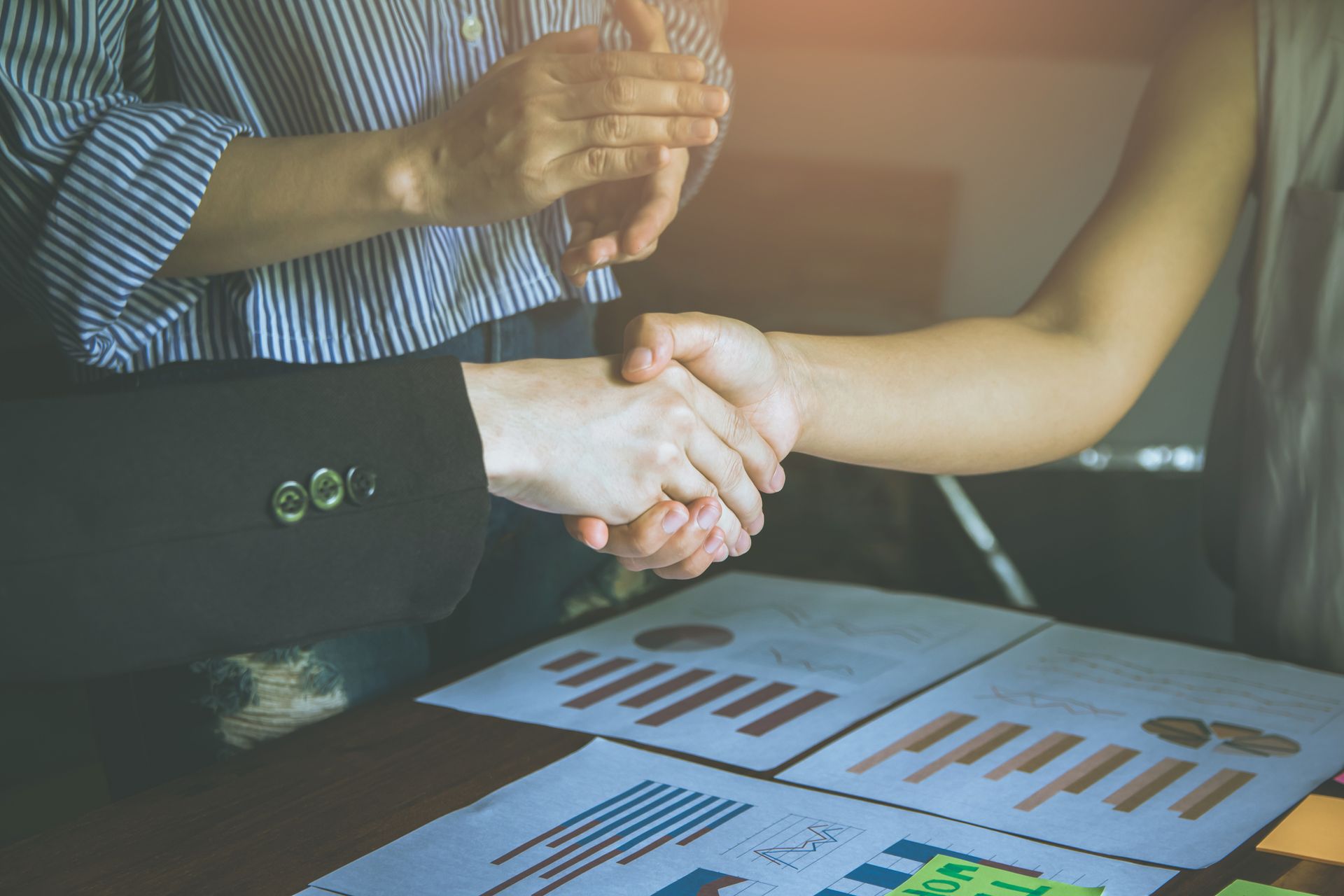 Two people shaking hands over a table with financial documents; one person clapping.