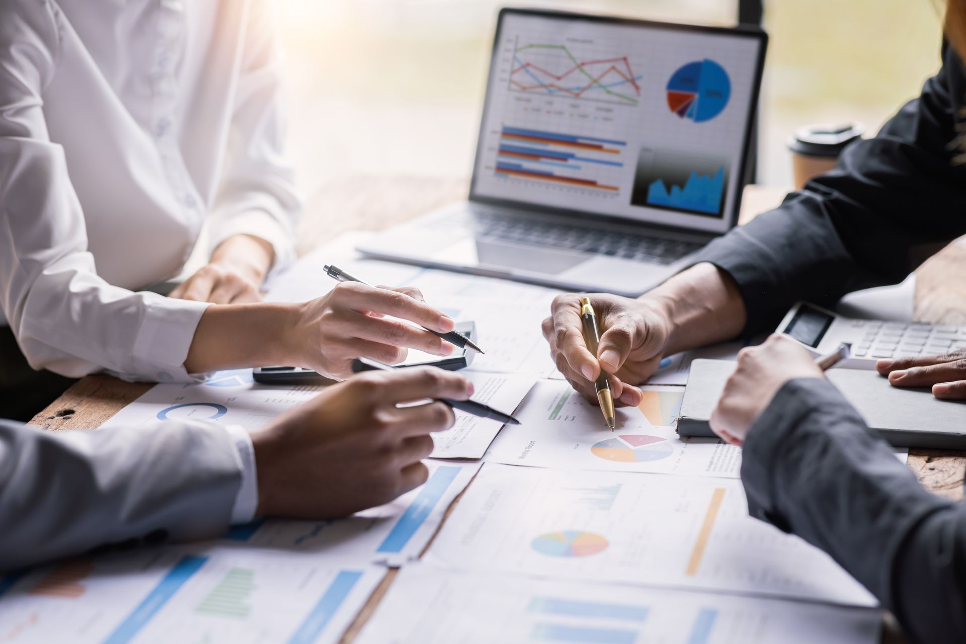 Business team analyzing charts and graphs on a laptop and documents, collaborating at a table.