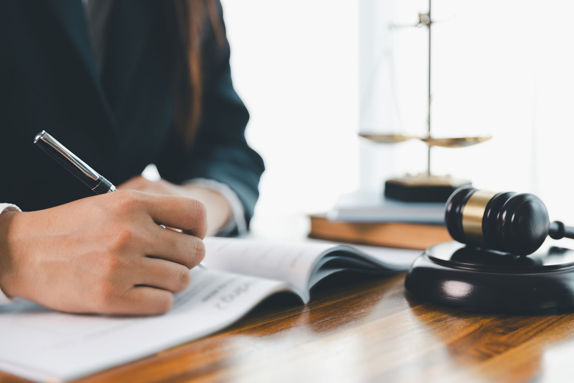 Person in suit writing on paper; gavel and scales on desk.
