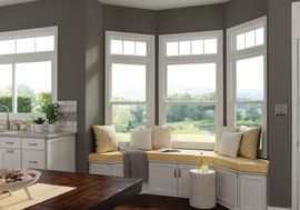 A kitchen bay window with built-in storage seating, yellow cushions, pillows, and white cabinets against dark gray walls.
