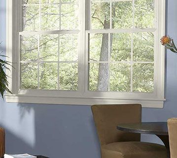 A window with a white frame and grid panes overlooks green trees, set against a periwinkle blue wall.