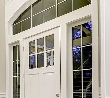 A white front entry door with a multi-pane glass window, an arched transom window above, and tall side panels.