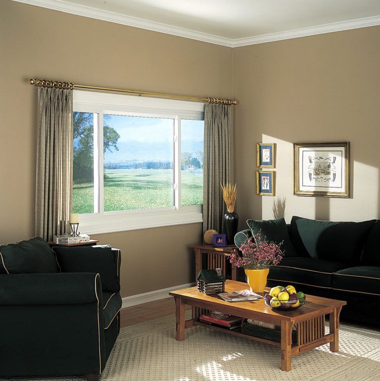 A living room with a large window, a dark sofa, an armchair, and a coffee table with a bowl of fruit and flowers.