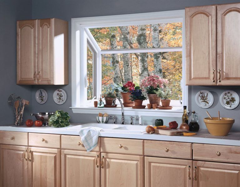 A kitchen sink area features a garden window filled with potted plants, light wood cabinets, and gray walls.