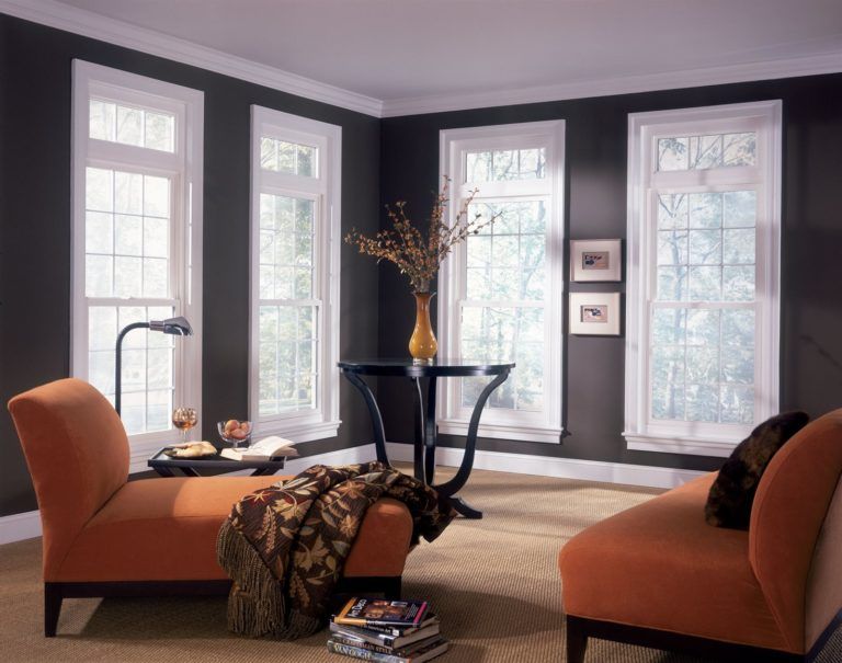 A room with dark gray walls, white-trimmed windows, two orange chaise lounges, and a small table with a vase in the corner.