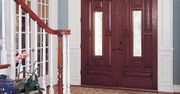 A dark wood double front door with glass panels, situated next to a white staircase in a home entryway.