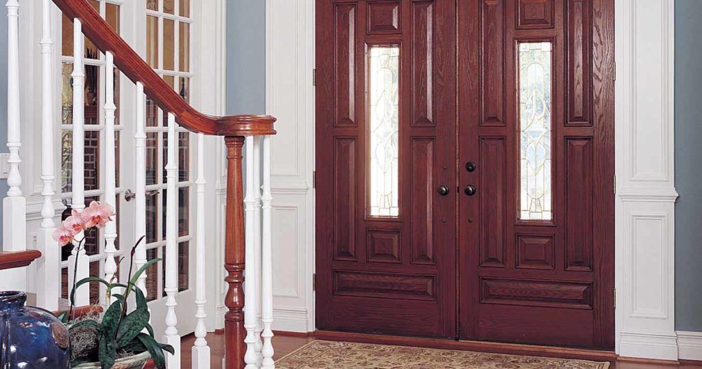 A dark wood double front door with glass panels, situated next to a white staircase in a home entryway.