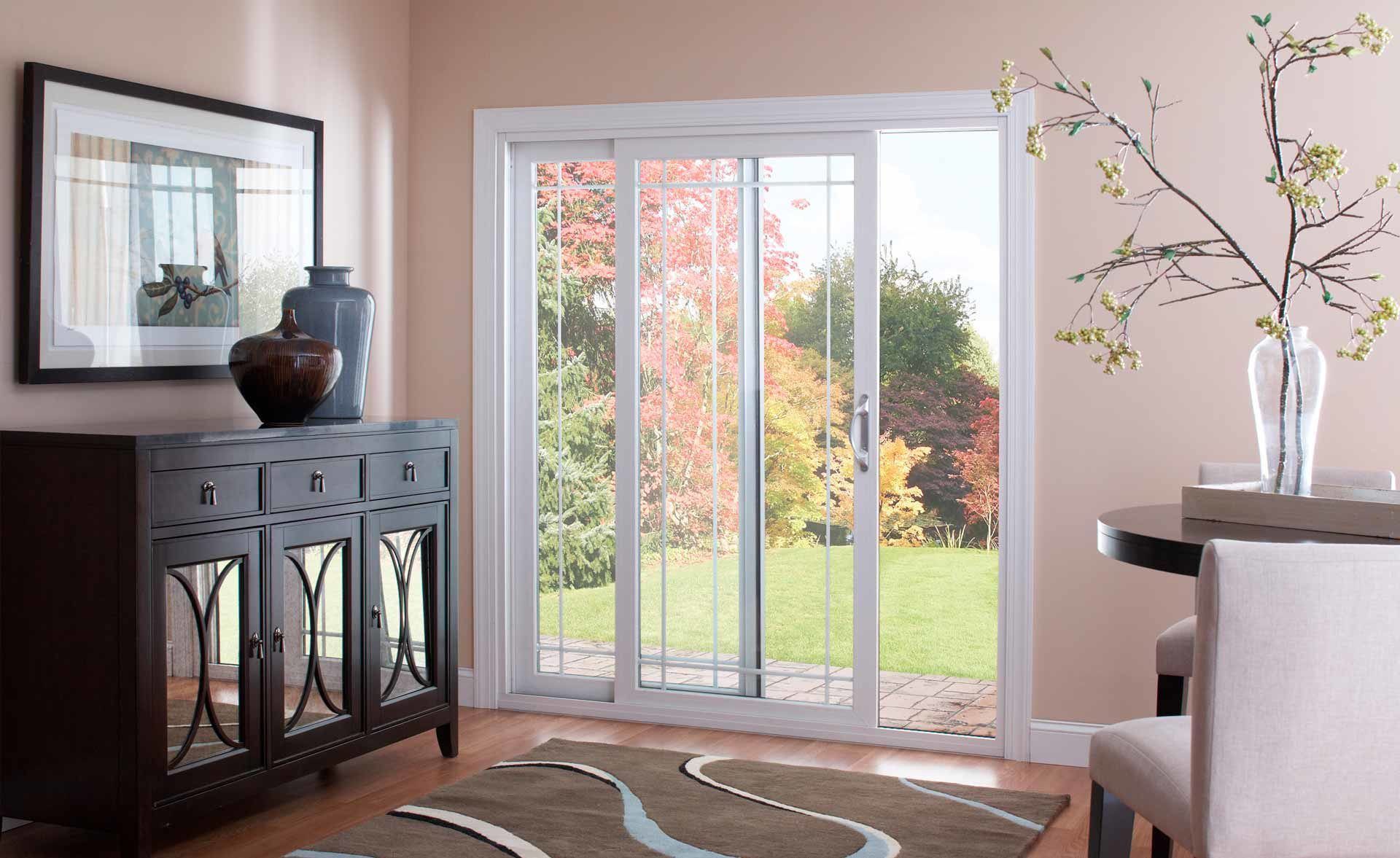 A bright room with a sliding glass door looking onto a leafy garden, a dark sideboard, and a table with floral branches.