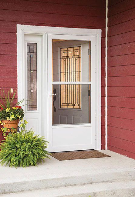 White screen door with a side window light and potted plants on a concrete porch against red horizontal siding.