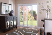 A sliding glass door opening to a yard, situated in a room with a dark sideboard, a dining chair, and a patterned rug.