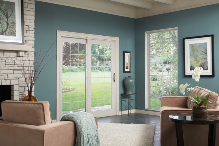 A cozy living room with teal walls, a stone fireplace, sliding glass doors, and two tan chairs facing each other.