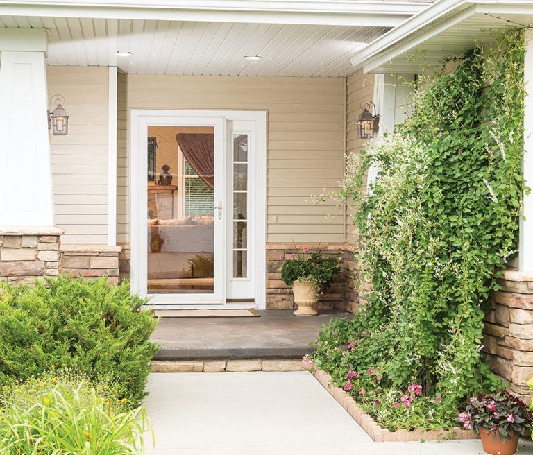 A beige house exterior with a white door, stone accents, and a front porch garden with climbing greenery.