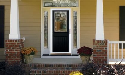 A black front door with a decorative glass panel, flanked by sidelights, on a tan home with brick porch pillars.