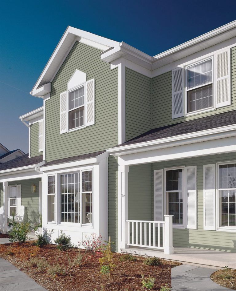 A sage green two-story house with white trim, white shutters, and a front porch, viewed from the yard.
