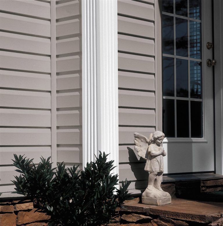 A small angel statue stands on a porch next to a white column and a glass-paneled door against beige siding.