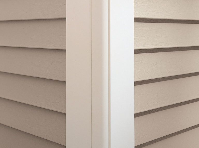 Close-up of the corner of a house showing beige horizontal vinyl siding meeting a white vertical corner trim post.
