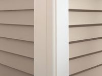Close-up of the corner of a house showing beige horizontal vinyl siding meeting a white vertical corner trim post.