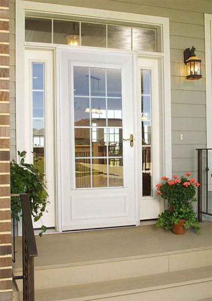 A white storm door with glass panes and side windows on a porch with potted plants, steps, and a wall-mounted lamp.
