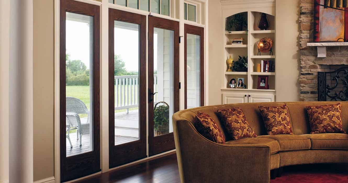 A living room with a curved sofa, a stone fireplace, built-in shelving, and dark-framed glass doors leading outside.