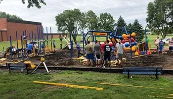 A group of people works together to assemble a new playground structure in a grassy outdoor area.