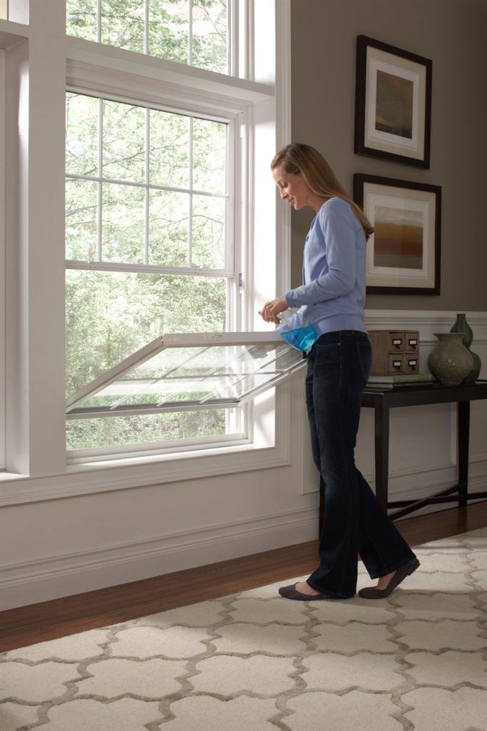 A person cleaning the inside of a tilted, double-hung window in a bright living room.