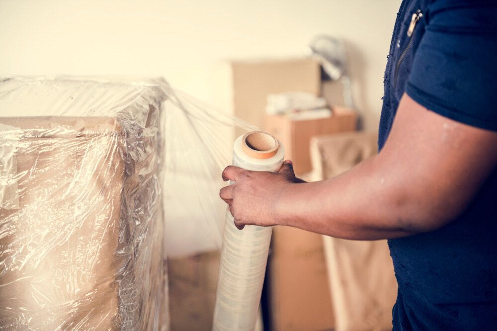 Person Wrapping Furniture in Clear Plastic Wrap During a Move — John's Furniture Removals in Buderim, QLD