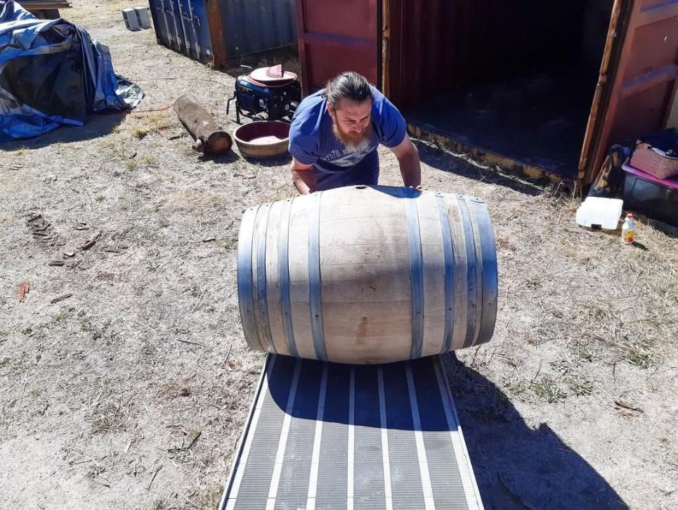 Man Rolling a Wooden Barrel on a Ramp Outside a Shipping Container — John's Furniture Removals in Yandina, QLD