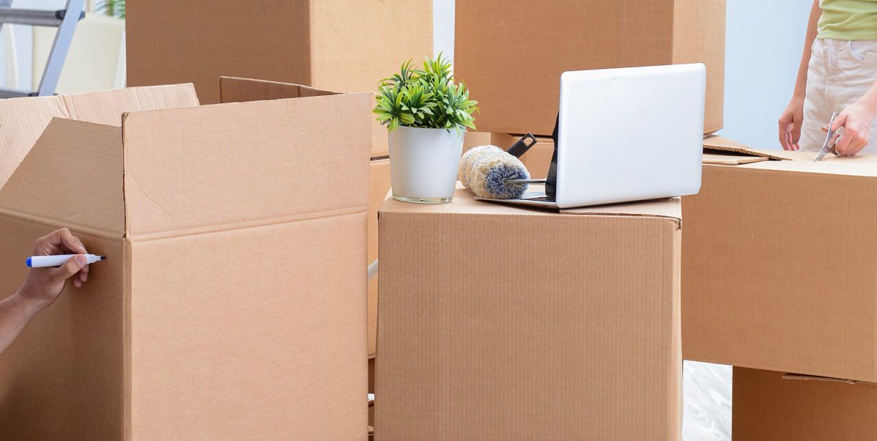 A Person in Blue Overalls Seals a Cardboard Box With Packing Tape — John's Furniture Removals in Caloundra, QLD