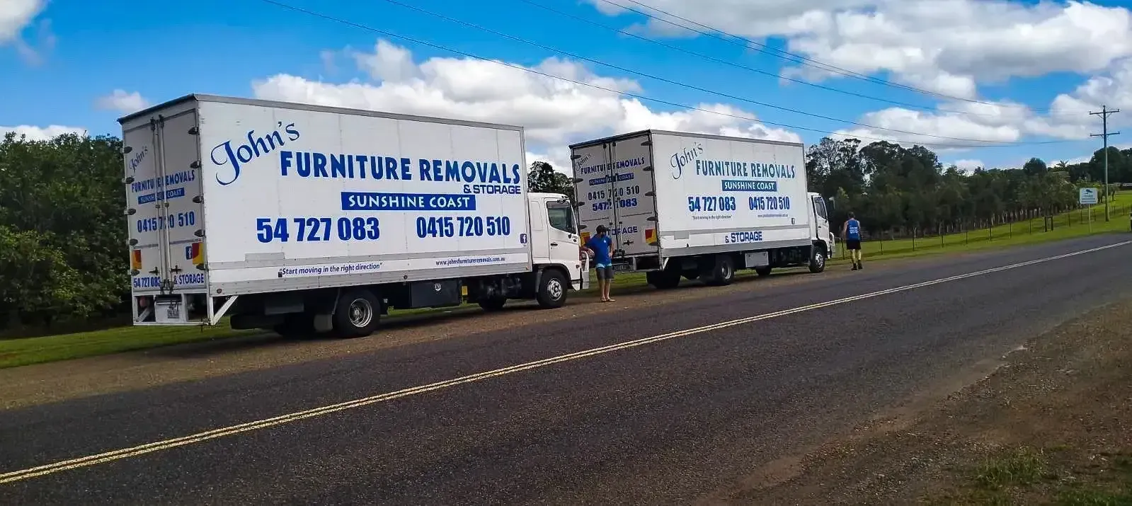 Two White Moving Trucks Parked on the Side of a Road Under a Blue Sky — John's Furniture Removals in Maroochydore, QLD