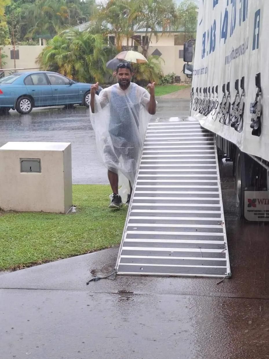 Man in Rain Poncho Gestures Thumbs-up Near Moving Truck Ramp on a Rainy Day — John's Furniture Removals in Yandina, QLD