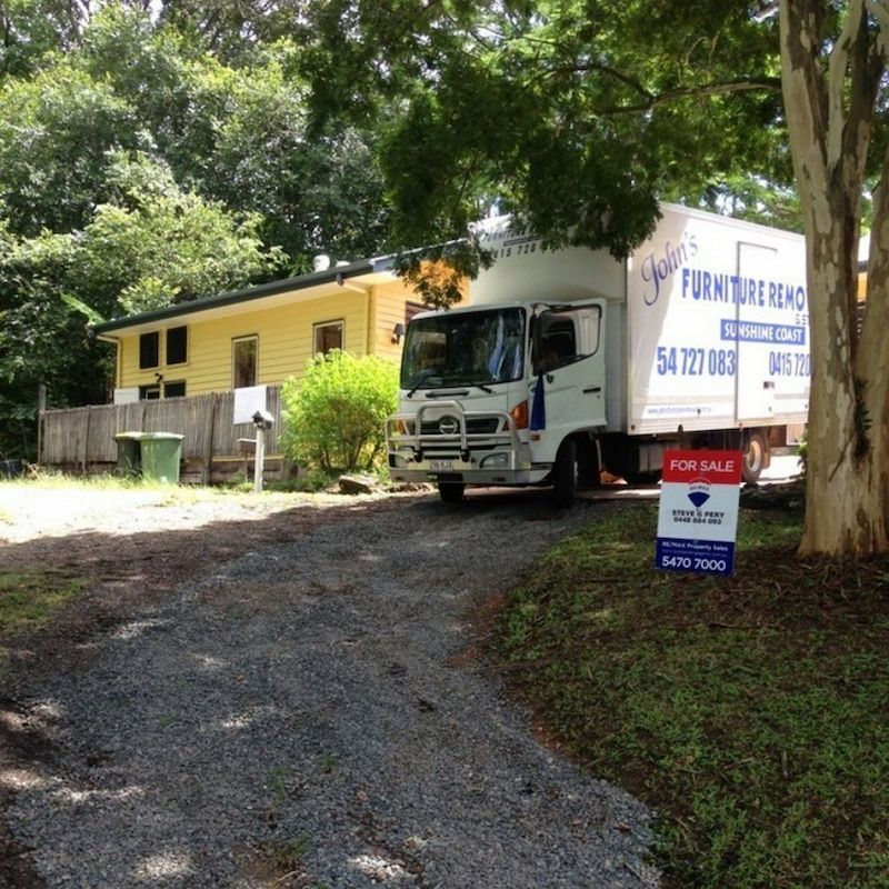 Moving Truck Parked in Driveway of Yellow House — John's Furniture Removals in Yandina, QLD