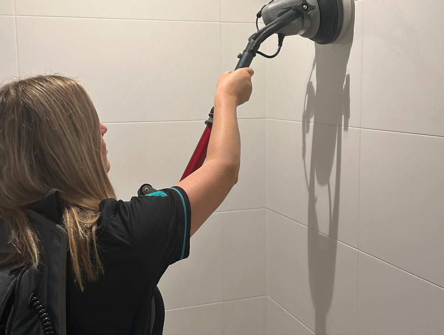 A Woman is Cleaning a White Tiled Wall With a Mop — Commercial Asset Maintenance In Coolum Beach, QLD