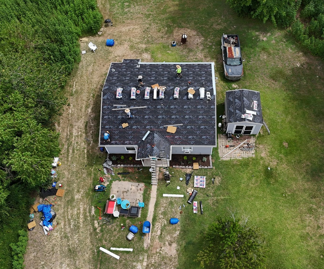 Aerial view of a house with roof replacement in progress, surrounded by tools, debris, and a parked truck.