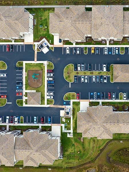 Aerial view of apartment complex with parking, playground, and green spaces.